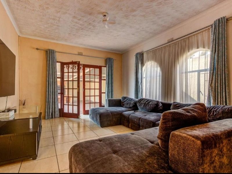 Spacious living room featuring tiled flooring, arched windows, and direct access to the patio through classic french doors.