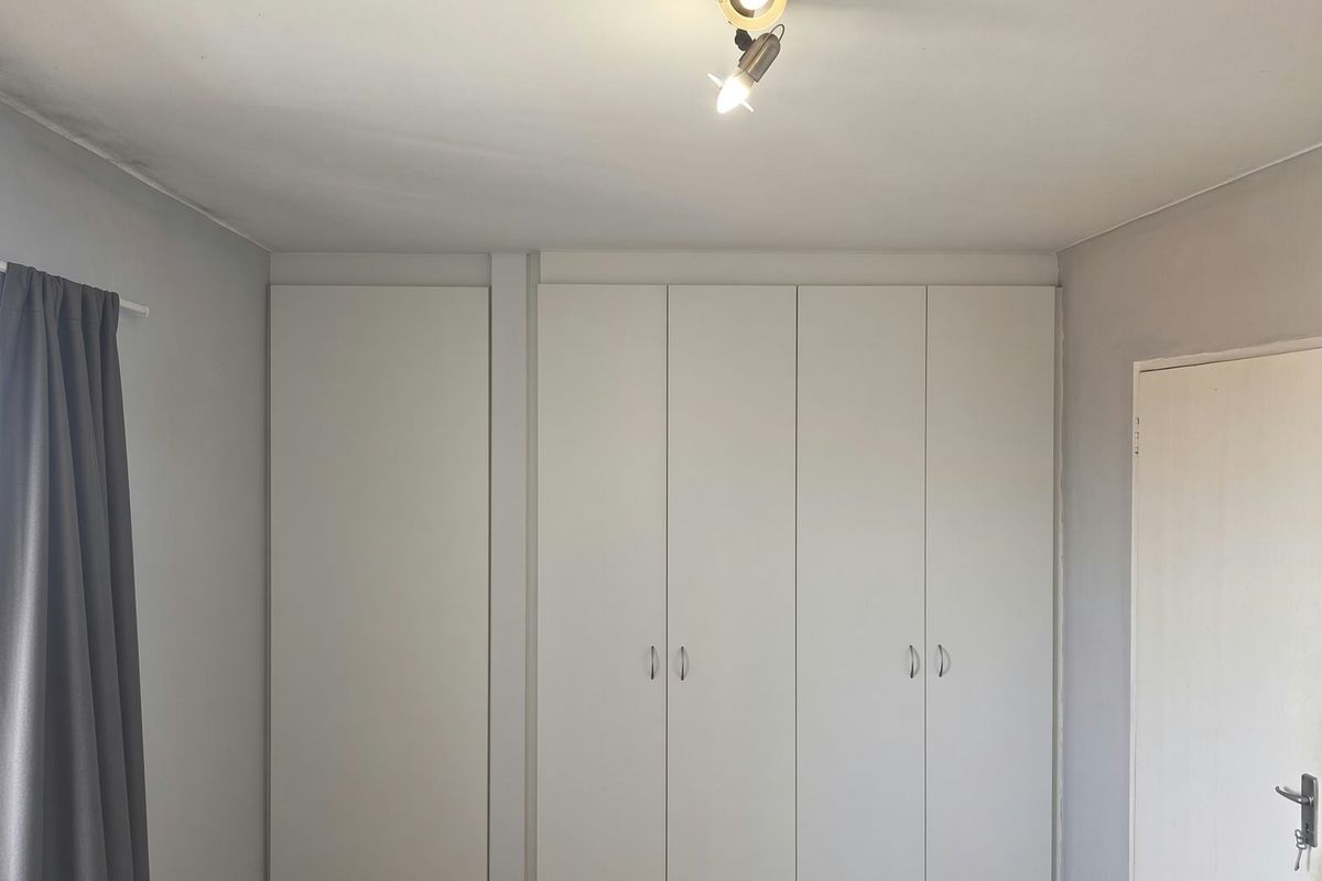 A clean, neutral bedroom featuring ample built-in cupboard storage and modern ceiling spotlighting.