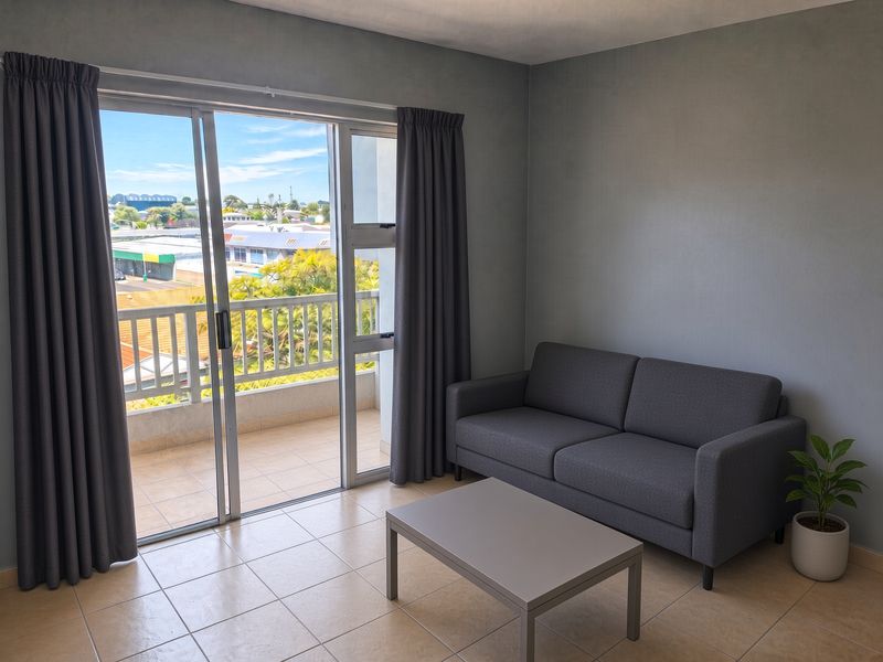 A bright living room featuring tiled flooring and a sliding glass door that opens onto a private balcony with neighborhood views.