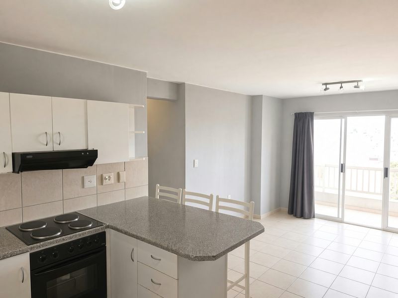 Open-plan kitchen and living area featuring tiled floors, built-in cabinetry, a breakfast bar, and sliding glass doors leading to a balcony.