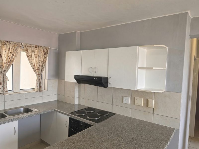 A functional kitchen featuring white cabinetry, laminate countertops, a built-in electric hob, oven, and a tiled backsplash with a stainless steel sink.