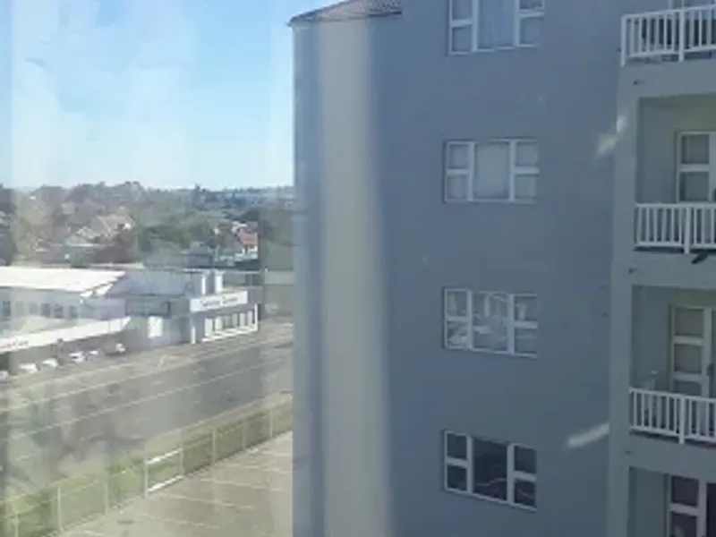 View from an apartment window overlooking a neighboring multi-story residential building and street level parking area.
