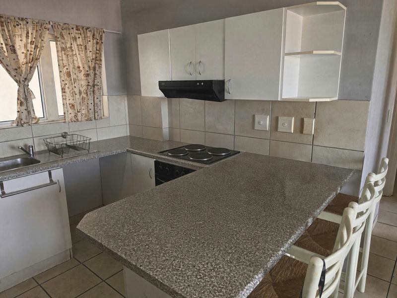 Functional kitchen featuring laminate countertops, built-in cabinetry, electric hob, oven, extractor fan, and tiled backsplash with a breakfast bar area.