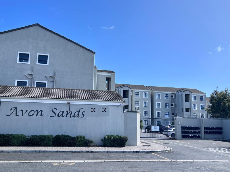 Front elevation of the Avon Sands apartment complex, featuring a secure gated entrance, paved driveway, and multi-story residential building blocks.