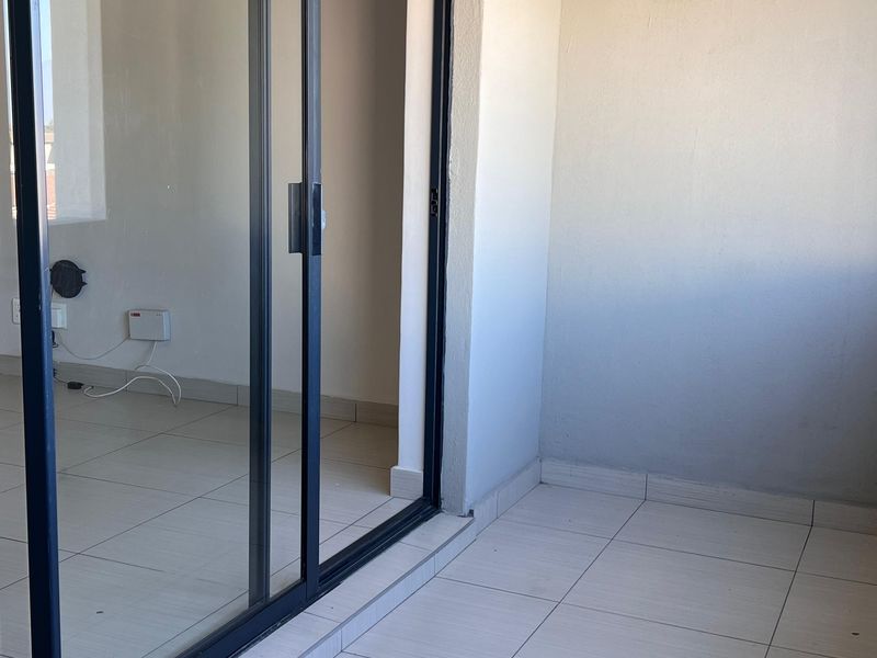 A clean, empty balcony featuring tiled flooring and a modern sliding glass door, providing a seamless transition to the interior living space.