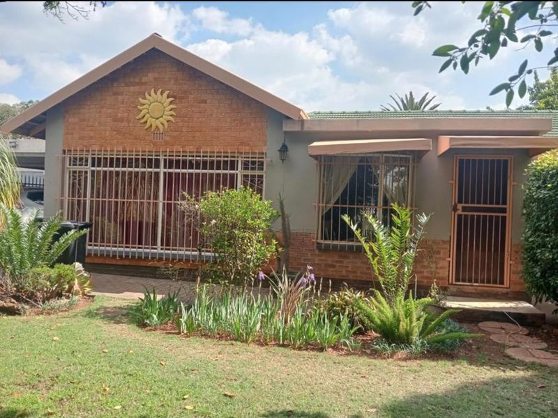 Front elevation of a single-story house featuring a brick facade, security bars on windows, a security gate, and a landscaped front garden.