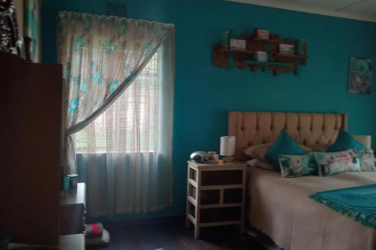 A bedroom featuring dark laminate flooring, a ceiling fan, and a window with curtain fixtures.