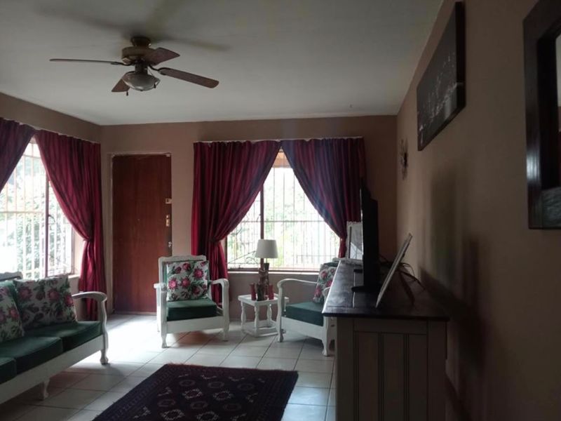 A living room featuring tiled flooring, a ceiling fan, and windows fitted with security bars.
