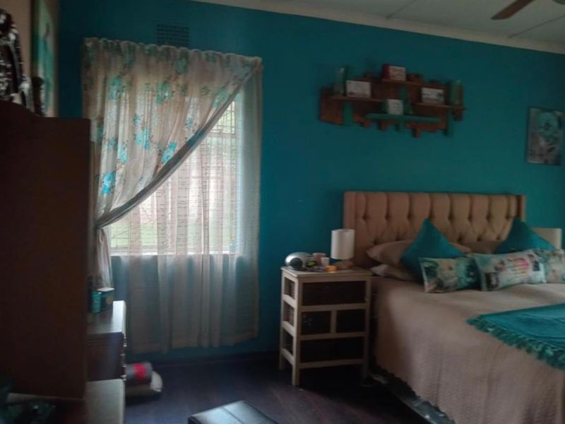 A bedroom featuring dark laminate flooring, a ceiling fan, and a window with curtain fixtures.