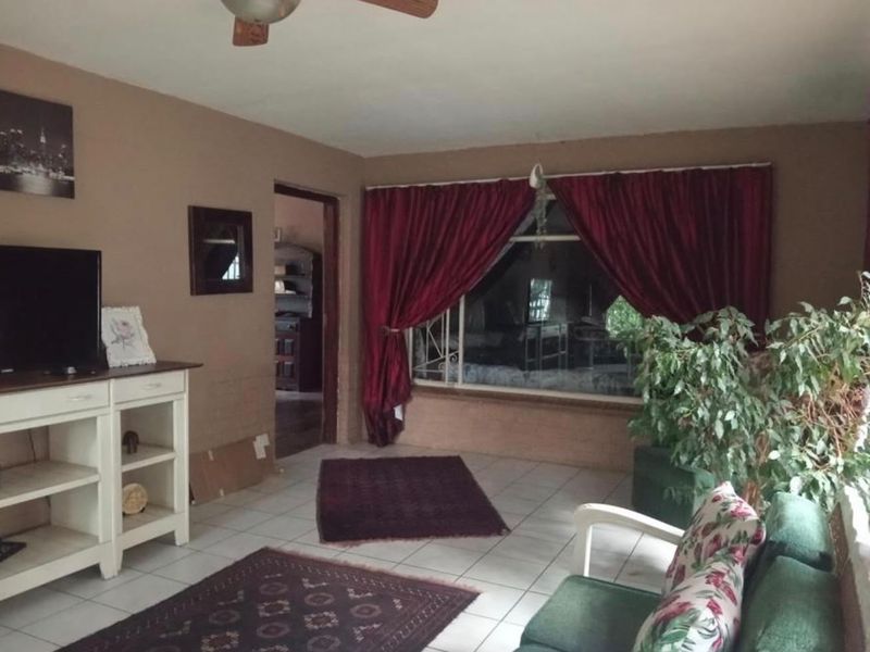 A living room featuring tiled flooring and a ceiling fan, with a large window covered by curtains.