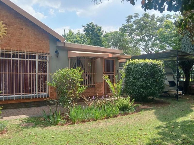 Front view of a brick-faced house featuring security bars on windows, a covered entrance, and an adjacent carport set within a landscaped garden.