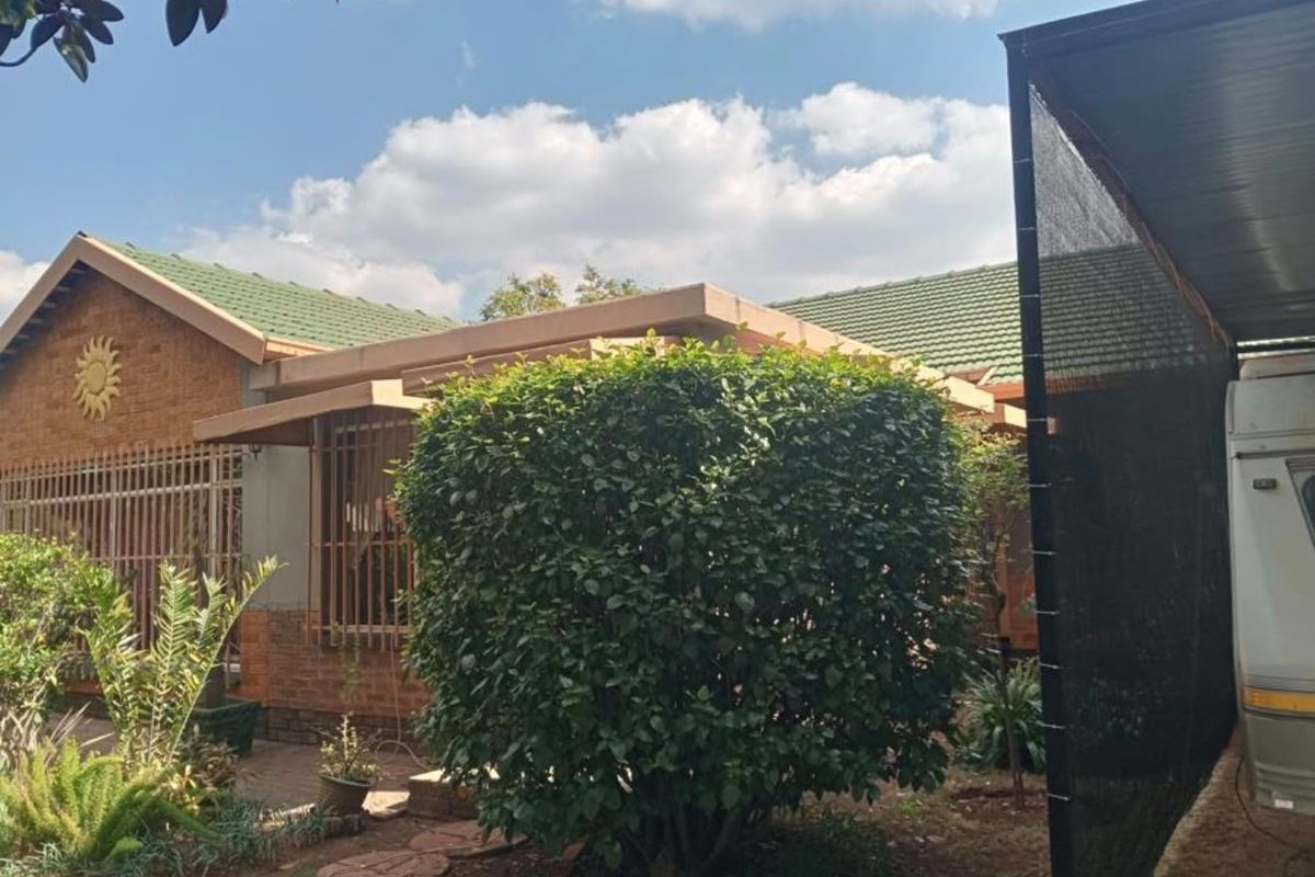 Rear exterior view of the house featuring a tiled roof, brick facade, and a covered carport area with established garden landscaping.