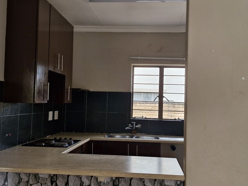 A functional kitchen featuring dark cabinetry, laminate countertops, a double bowl sink, and a built-in hob, offering a practical layout for daily use.