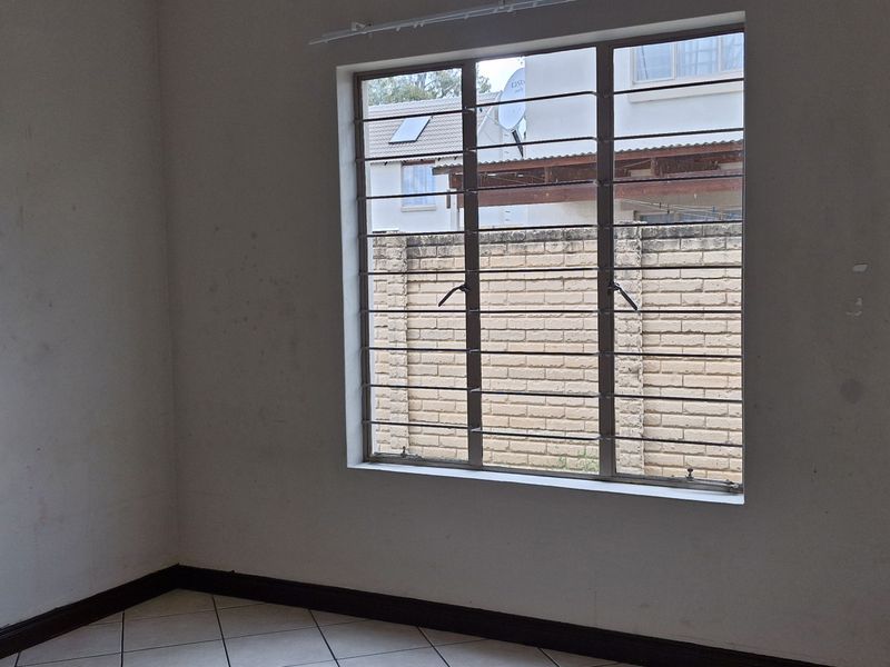 An empty bedroom featuring tiled flooring and a window fitted with security bars, requiring minor cosmetic attention to the walls.