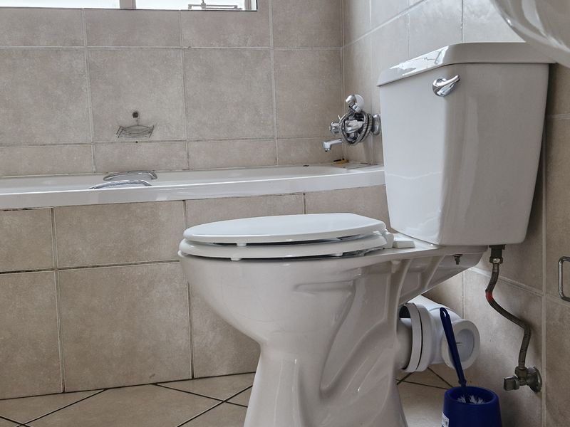 A functional bathroom featuring a bathtub, pedestal basin, and toilet with neutral wall and floor tiling.