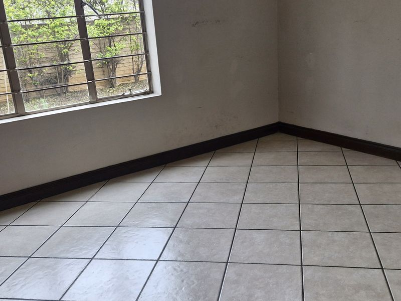 An empty bedroom featuring neutral floor tiles, dark skirting boards, and a window fitted with security burglar bars.