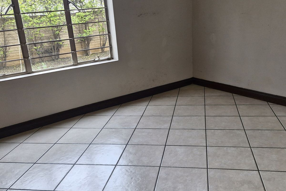 An empty bedroom featuring neutral floor tiles, dark skirting boards, and a window fitted with security burglar bars.