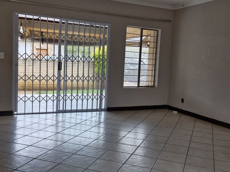 An empty living room featuring ceramic floor tiles, a sliding glass door with a security gate, and window security bars.