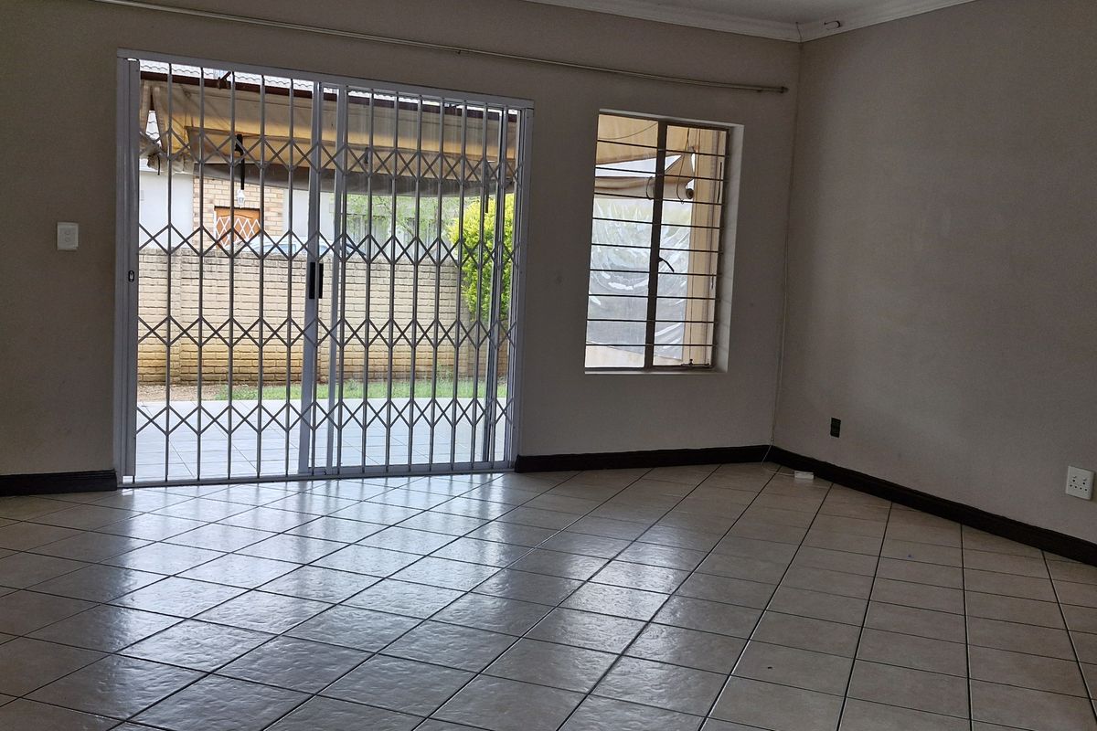 An empty living room featuring ceramic floor tiles, a sliding glass door with a security gate, and window security bars.