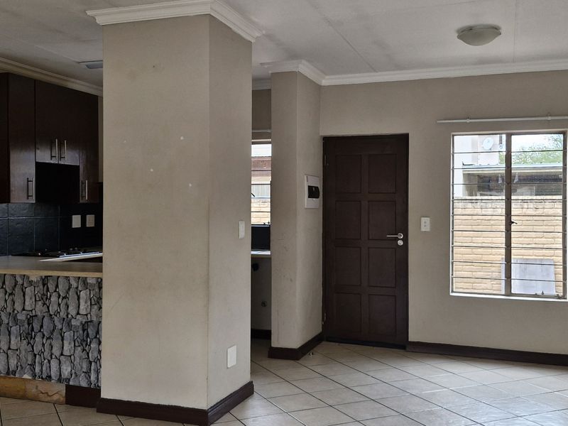 Open-plan living and kitchen area featuring tiled floors, stone-cladded breakfast counter, built-in cabinetry, and security bars on the window.