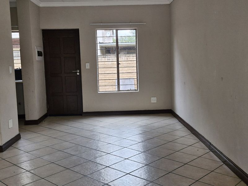 An empty open-plan living area featuring tiled flooring, neutral wall tones, and a secure window, providing a blank canvas for interior design.