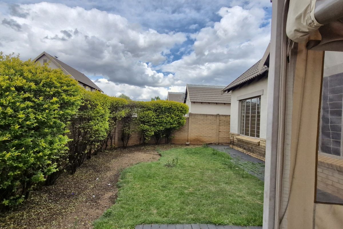 A private rear garden featuring a lawn, paved patio area, and established boundary hedging, providing a functional outdoor space for the townhouse.