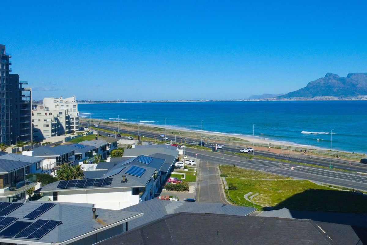 A panoramic coastal view overlooking the ocean, beach, and distant mountains, showcasing the prime location of the property.