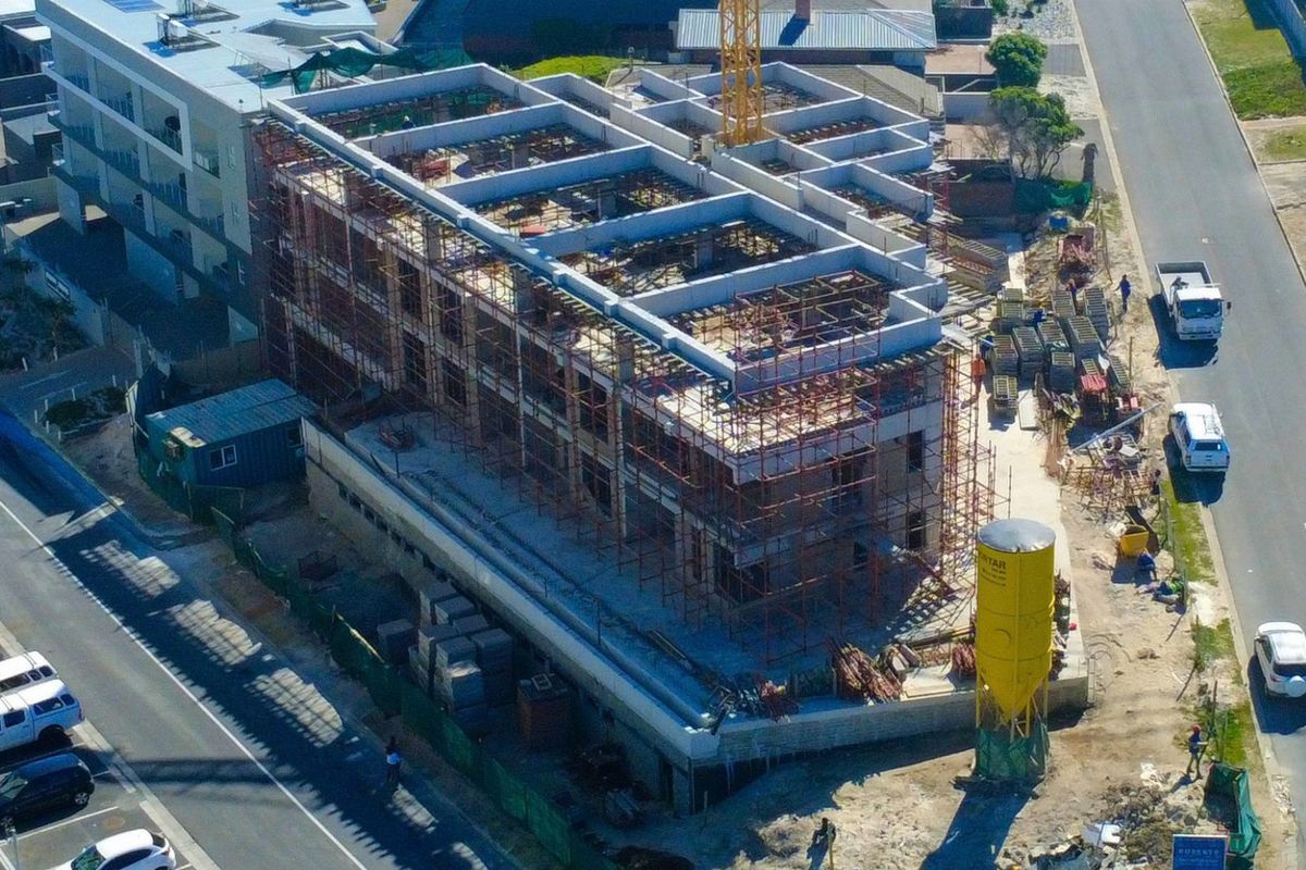 Aerial view of a multi-story apartment building currently under construction, featuring a concrete frame, scaffolding, and site equipment.