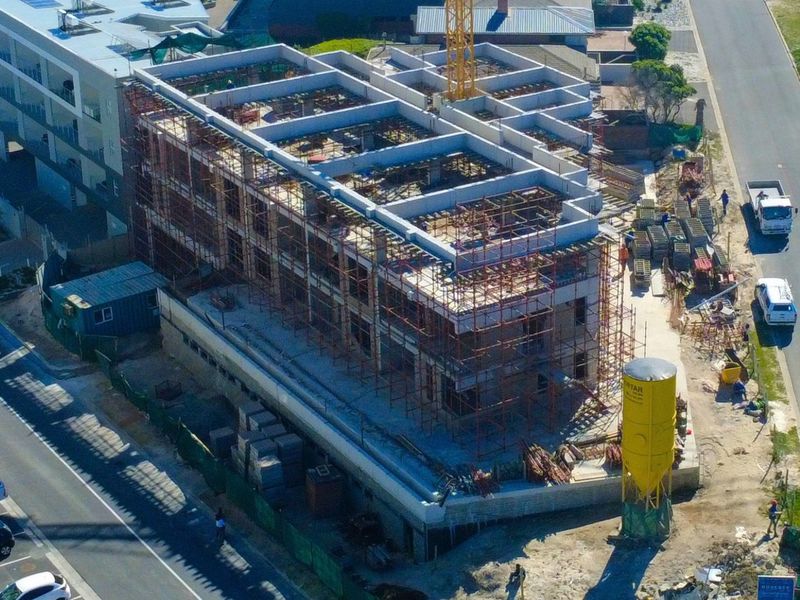 Aerial view of a multi-story apartment building currently under construction, featuring a concrete frame, scaffolding, and site equipment.