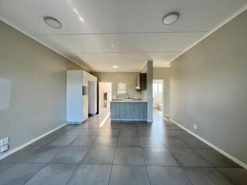 An open-plan living and kitchen area featuring neutral wall tones, large format floor tiles, and a central kitchen island with built-in cabinetry.