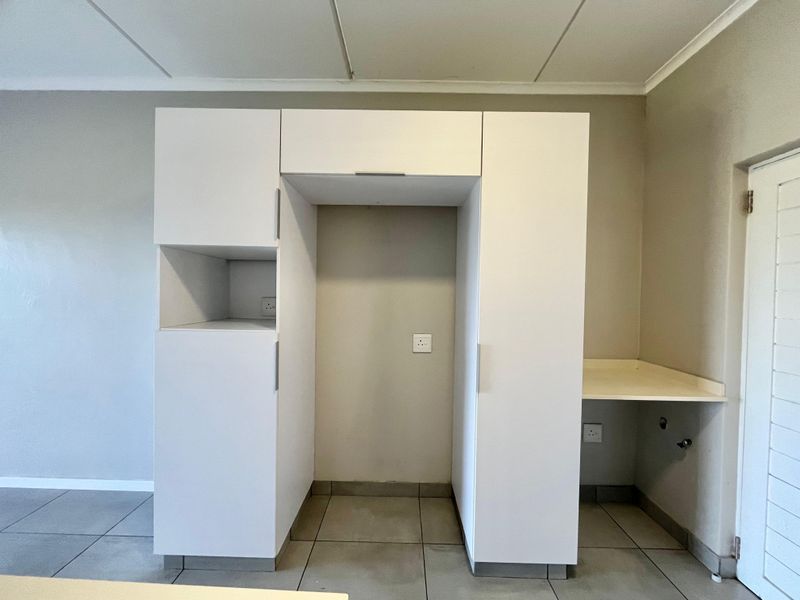A clean, modern kitchen area featuring white built-in cabinetry, tiled flooring, and dedicated appliance recesses with integrated plumbing and electrical connections.