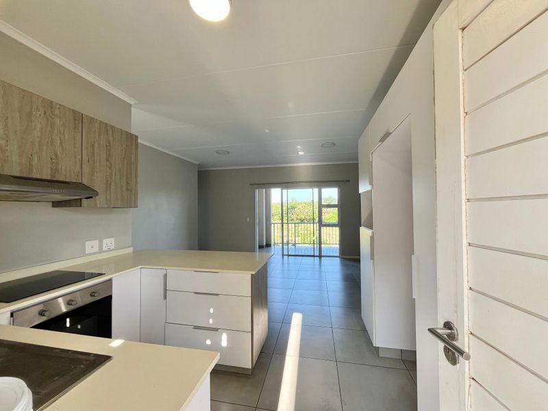 Modern open-plan kitchen and living area featuring tiled floors, sleek cabinetry, built-in appliances, and direct access to a balcony.