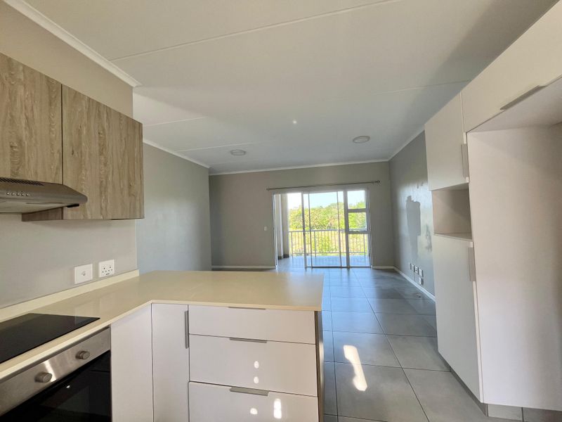 Modern open-plan kitchen and living area featuring sleek cabinetry, built-in appliances, tiled floors, and direct access to a balcony with natural light.