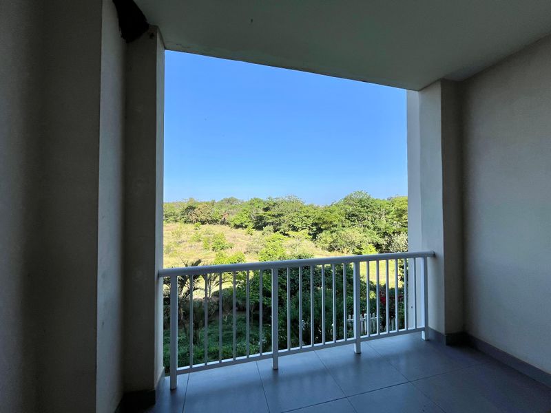 A covered balcony featuring tiled flooring and a white metal balustrade, offering an open view of the surrounding greenery.