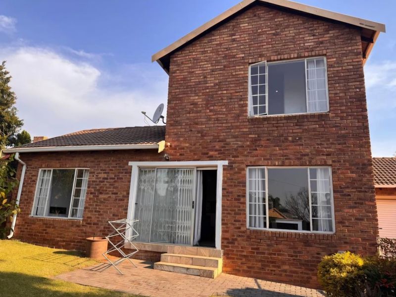 Rear view of a double-story face brick townhouse featuring a paved patio, sliding door access, and established garden area.