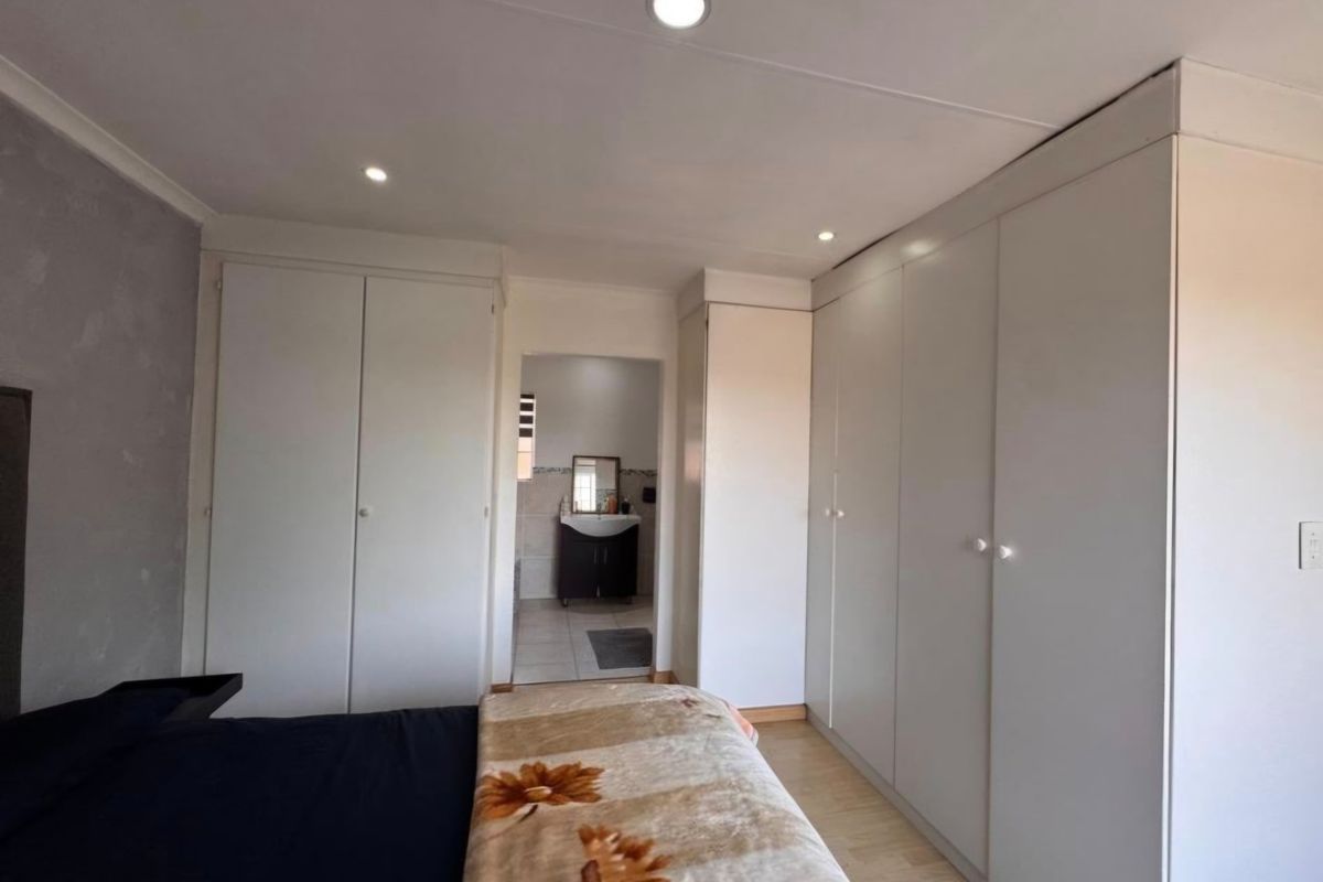 A well-maintained bedroom featuring extensive built-in cupboards, recessed downlighting, laminate flooring, and direct access to an en-suite bathroom.