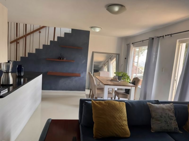 Open plan living and dining area featuring a modern staircase, floating shelves, and a kitchen island with a stone countertop.