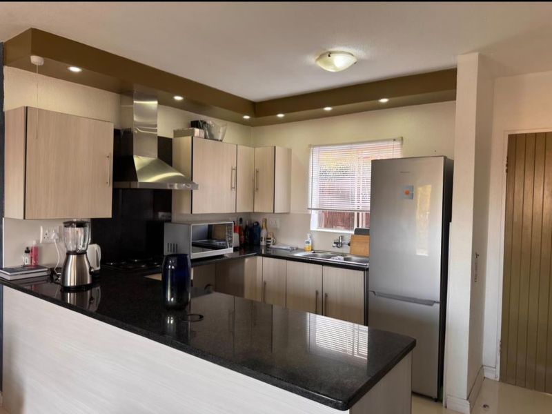A functional kitchen featuring granite countertops, light wood-finish cabinetry, a stainless steel extractor fan, and recessed lighting, offering a clean and practical workspace.
