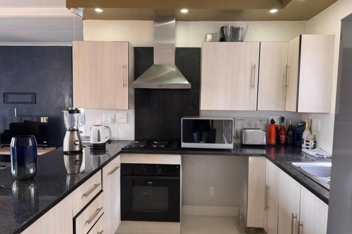 Functional kitchen featuring granite countertops, built-in oven, extractor fan, and light-toned cabinetry, offering a practical layout for daily meal preparation.