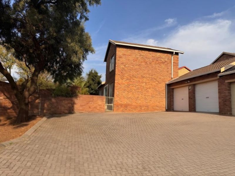 Exterior view of a face-brick townhouse featuring a paved driveway and double garage with roller doors.
