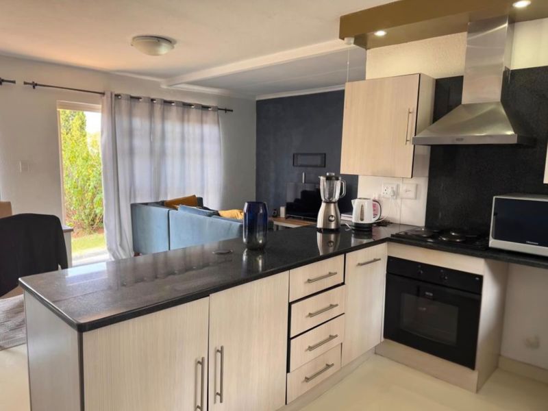 Open-plan kitchen and living area featuring modern granite countertops, built-in oven, gas hob, and direct access to the outdoor space via sliding glass doors.