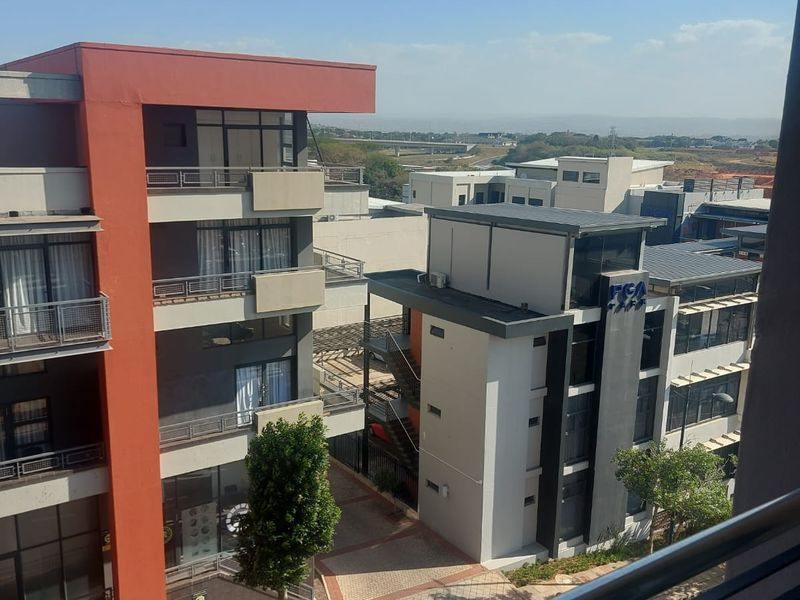 An elevated view from a balcony overlooking the surrounding apartment complex, paved walkways, and modern building architecture.