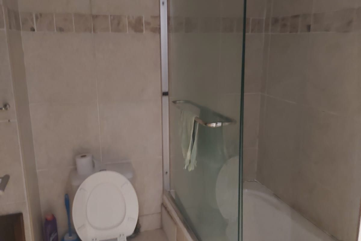 A compact bathroom featuring a standard toilet and a bathtub with a glass shower screen, finished with neutral wall and floor tiling.