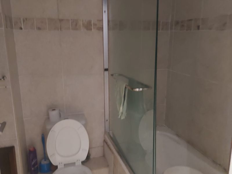 A compact bathroom featuring a standard toilet and a bathtub with a glass shower screen, finished with neutral wall and floor tiling.