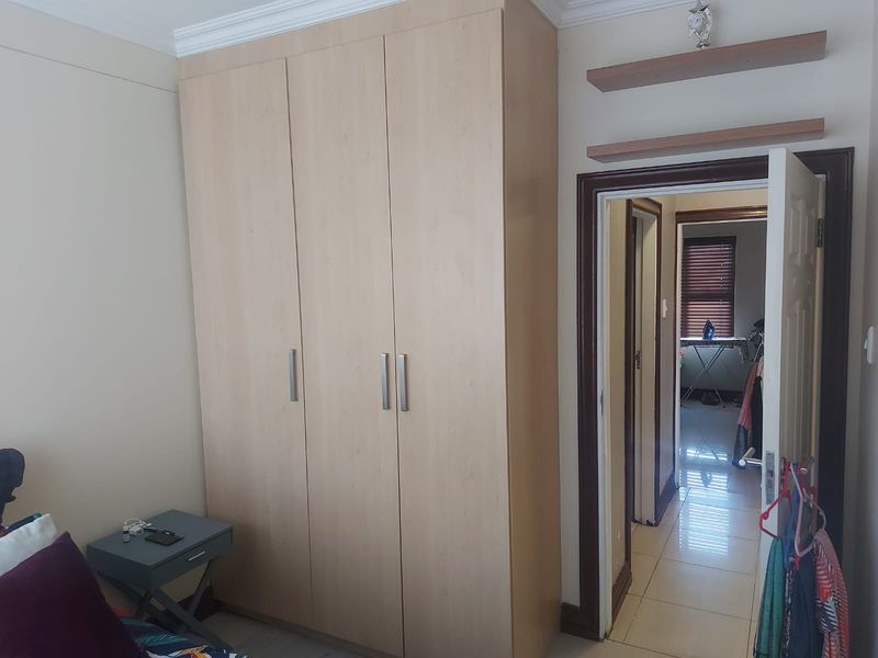 A bedroom featuring a light wood built-in wardrobe, floating wall shelves, and crown molding, with a view into the adjacent hallway.