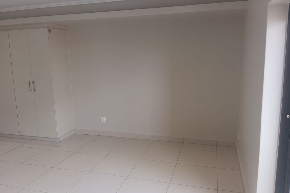 A clean, empty bedroom featuring neutral tiled flooring, built-in cupboards, and recessed ceiling lighting, providing a blank canvas for personalization.