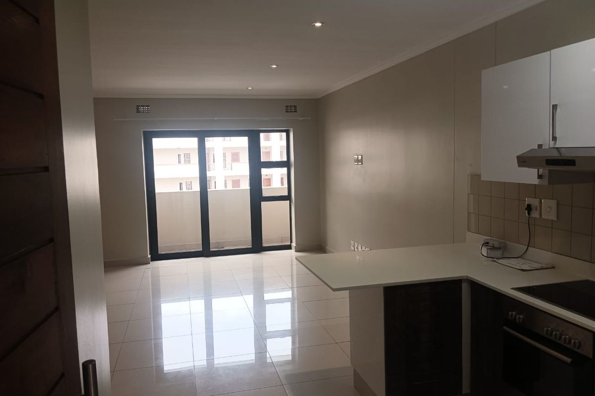An open-plan living and kitchen area featuring modern cabinetry, built-in appliances, tiled flooring, and a sliding glass door leading to a balcony.