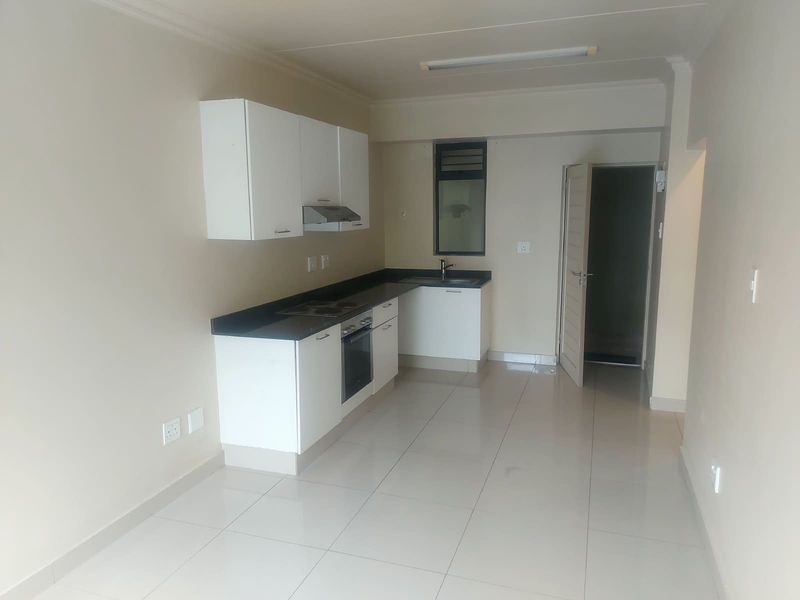 A clean, empty kitchen featuring white cabinetry, dark countertops, built-in oven and hob, and neutral tiled flooring.