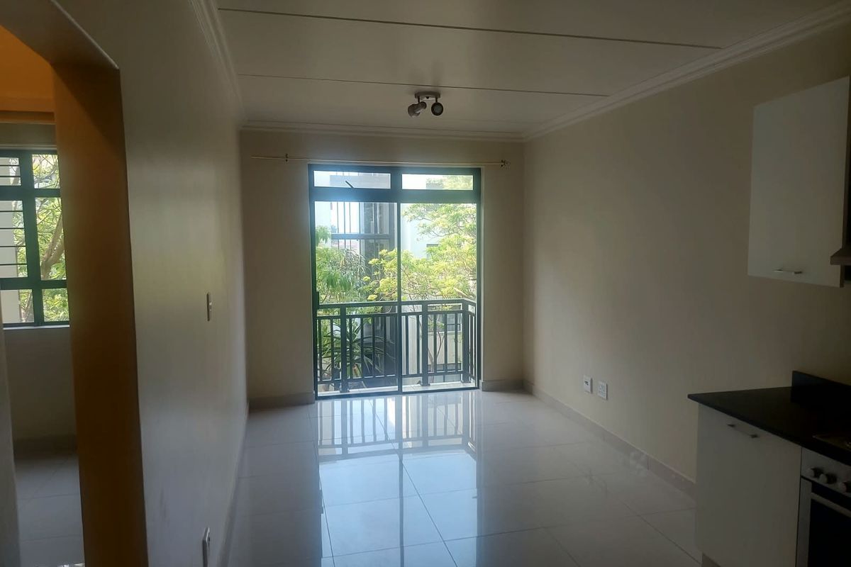 A bright, open-plan living and kitchen area featuring polished tile flooring, modern cabinetry, built-in oven, and direct access to a private balcony.