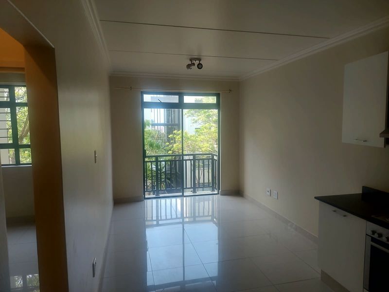 A bright, open-plan living and kitchen area featuring polished tile flooring, modern cabinetry, built-in oven, and direct access to a private balcony.